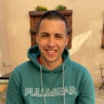 Photo of Domen outside, wearing a sweatshirt and smiling, with some plants behind him.